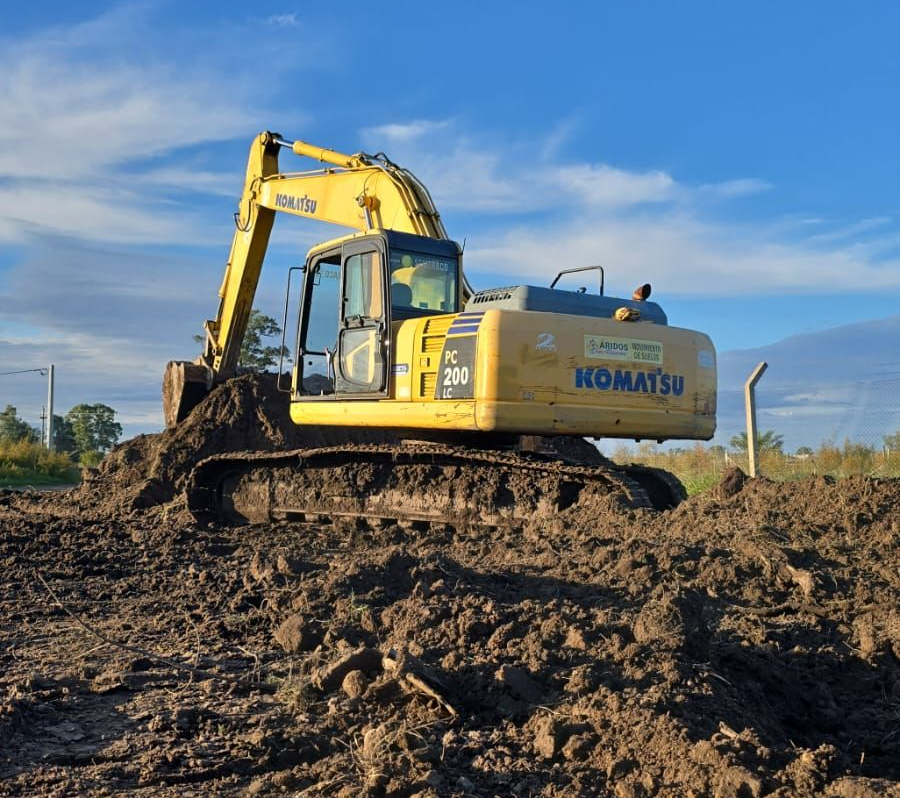 Excavadora Komatsu amarilla en una obra embarrada bajo un cielo azul