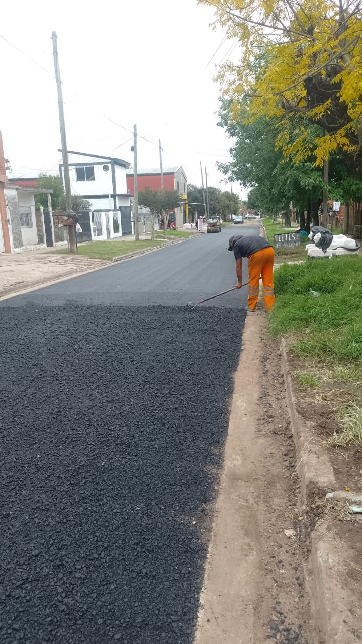 Un trabajador pavimenta una calle residencial junto a un arcén de tierra y unos árboles