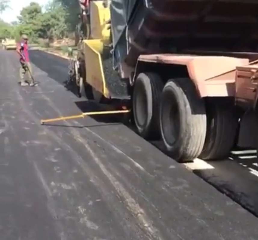 Máquina pavimentadora extendiendo asfalto en una autopista junto a un trabajador que sostiene un rastrillo.