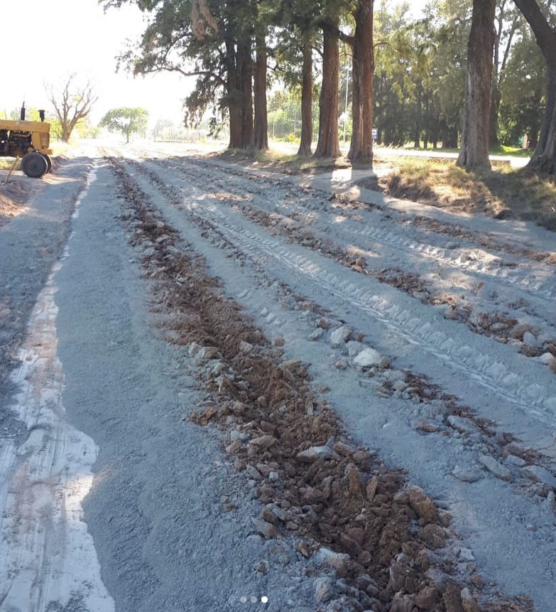 Carretera cubierta de nieve con huellas de neumáticos, árboles a los lados y un tractor en el extremo izquierdo.