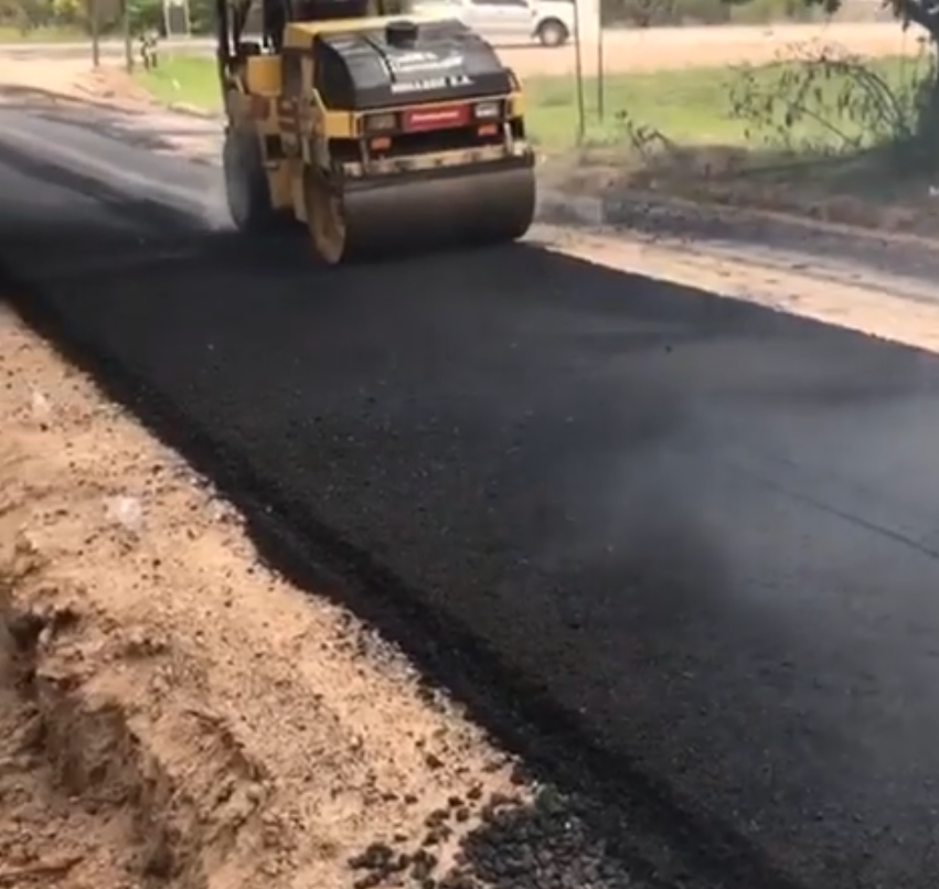 Una apisonadora está pavimentando un carril nuevo de asfalto negro junto a un arcén de tierra.