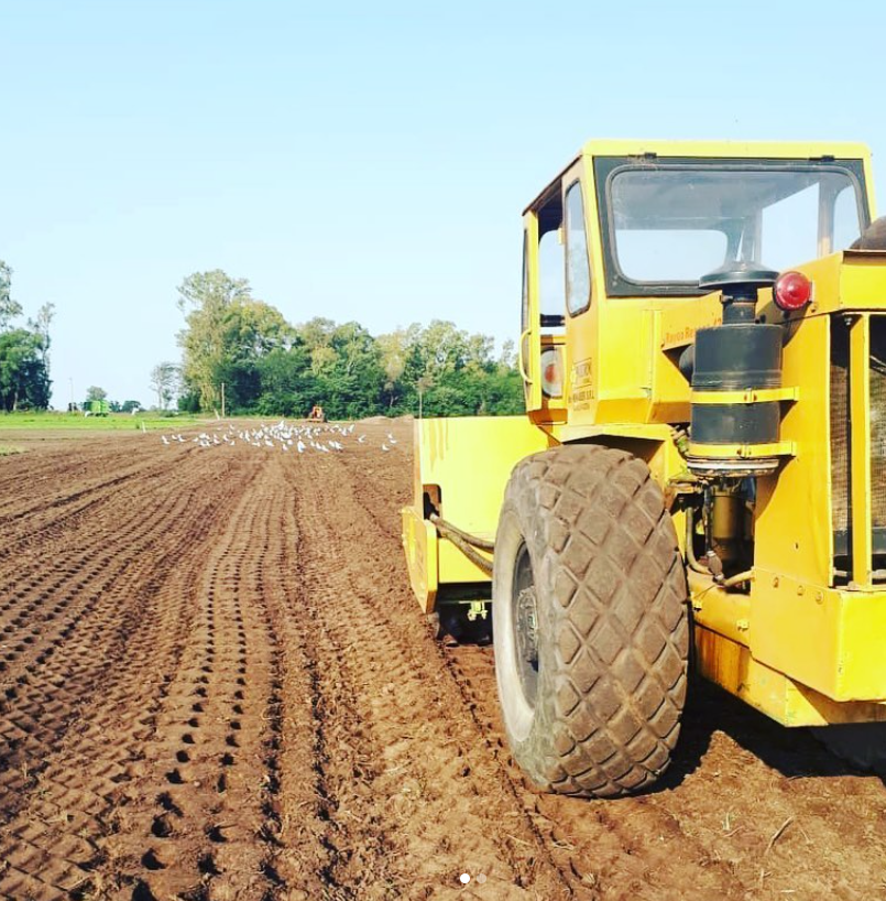 Tractor agrícola amarillo en un campo recién arado bajo un cielo azul despejado.