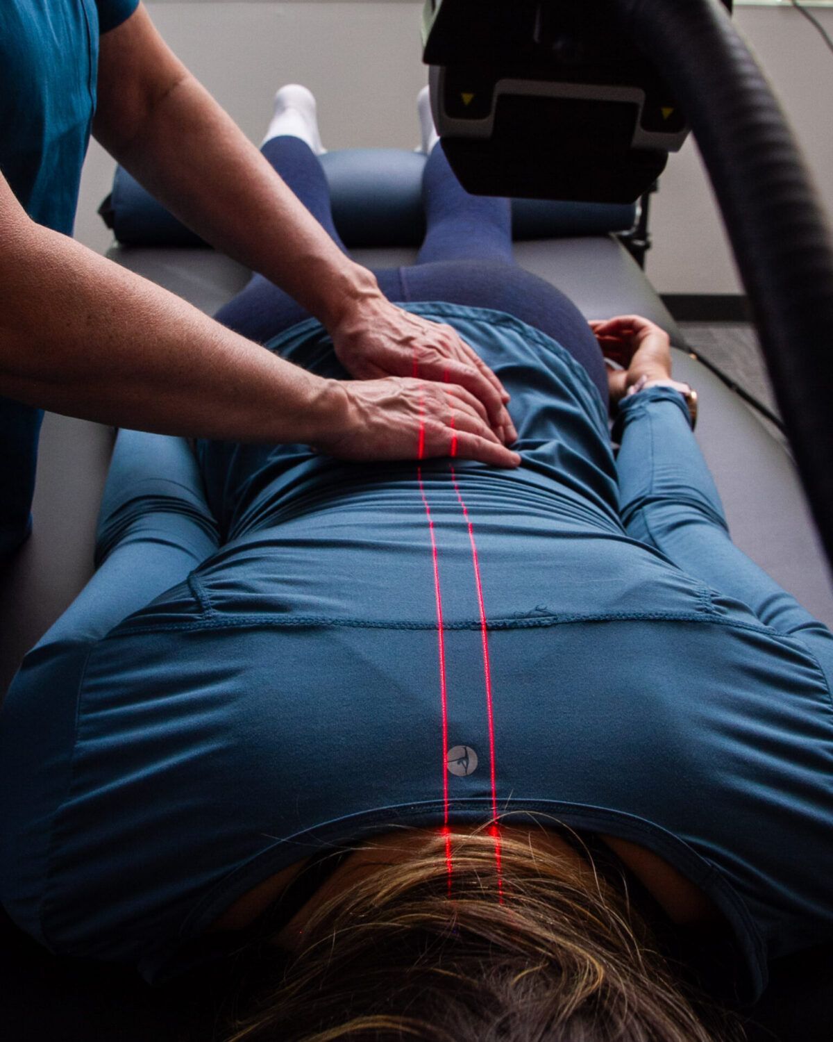 Chiropractor adjusting a patient's back. Red laser lines show spine alignment.