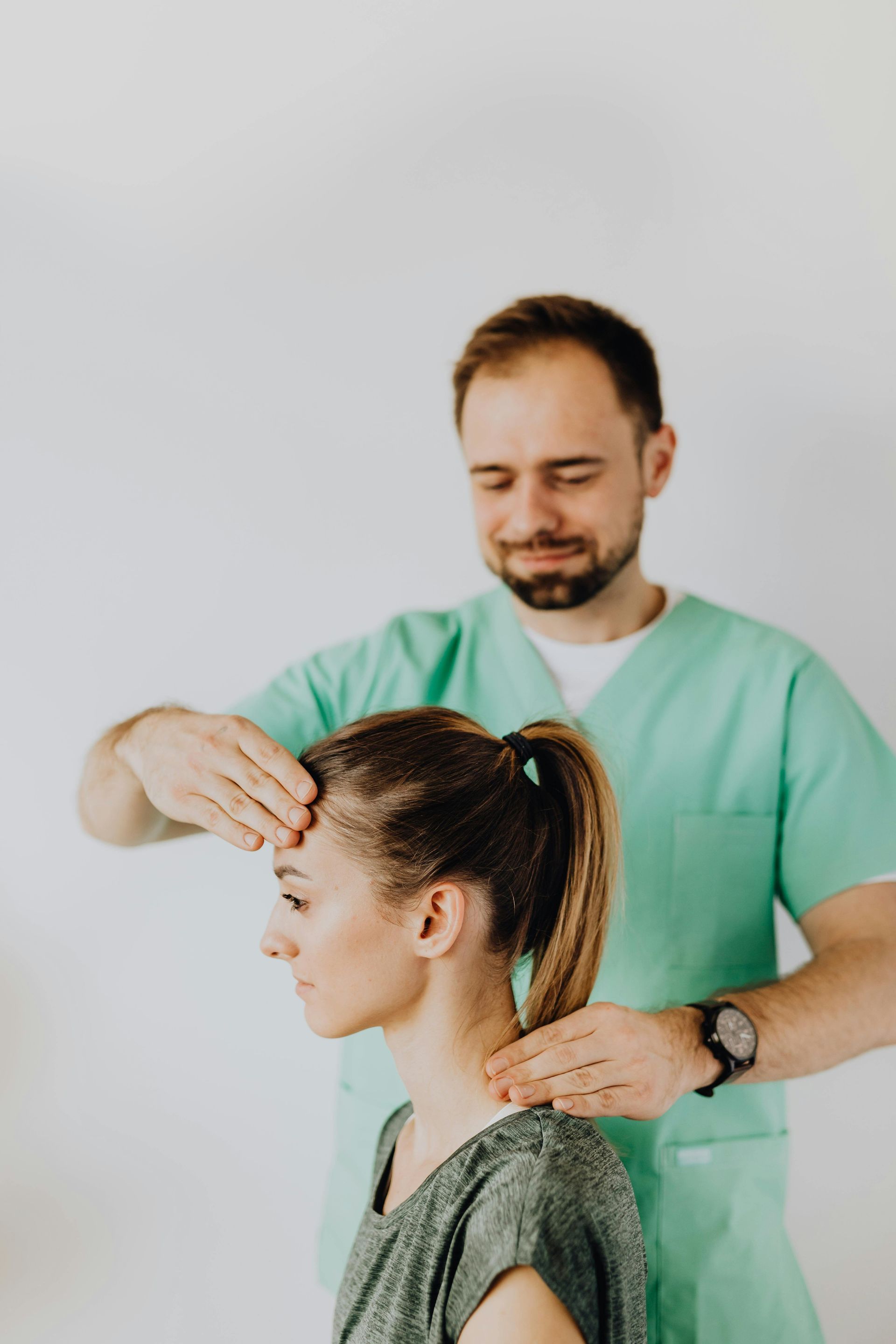 Man in scrubs examining a person's head and neck; white background.