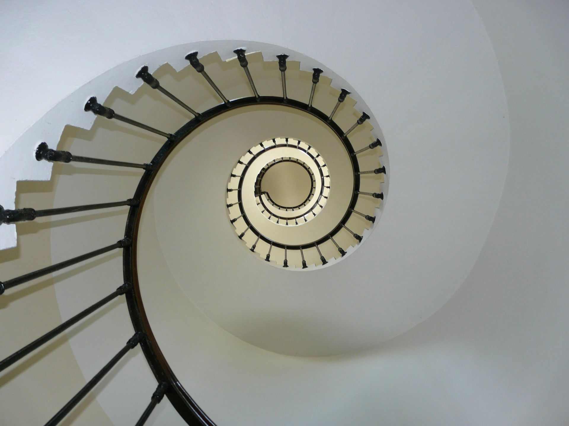 Spiral staircase, viewed from below, black railing, white walls, and stairs.