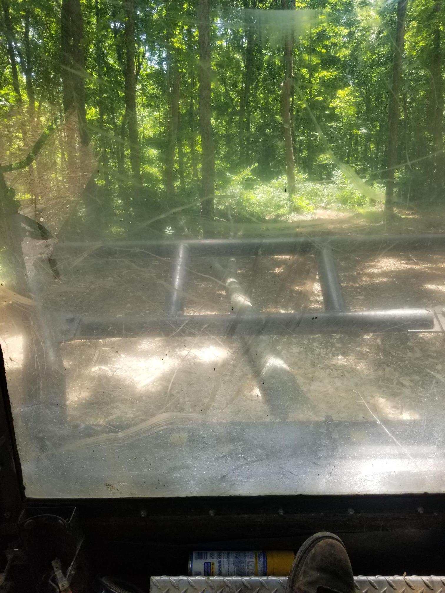 View from inside a vehicle looking through a windshield at a wooded area; foot on a diamond plate floor.