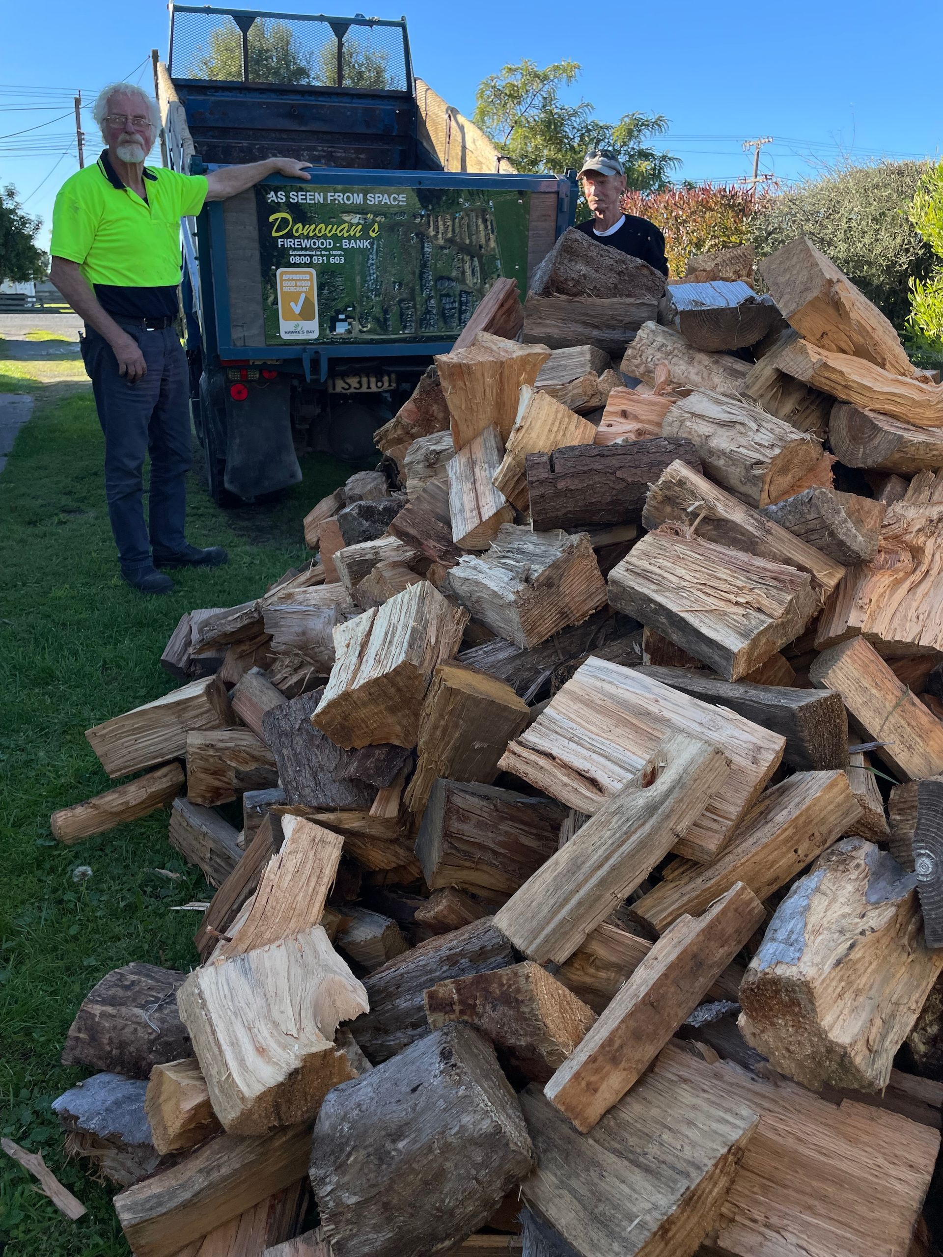 Two men are standing next to a pile of wood.