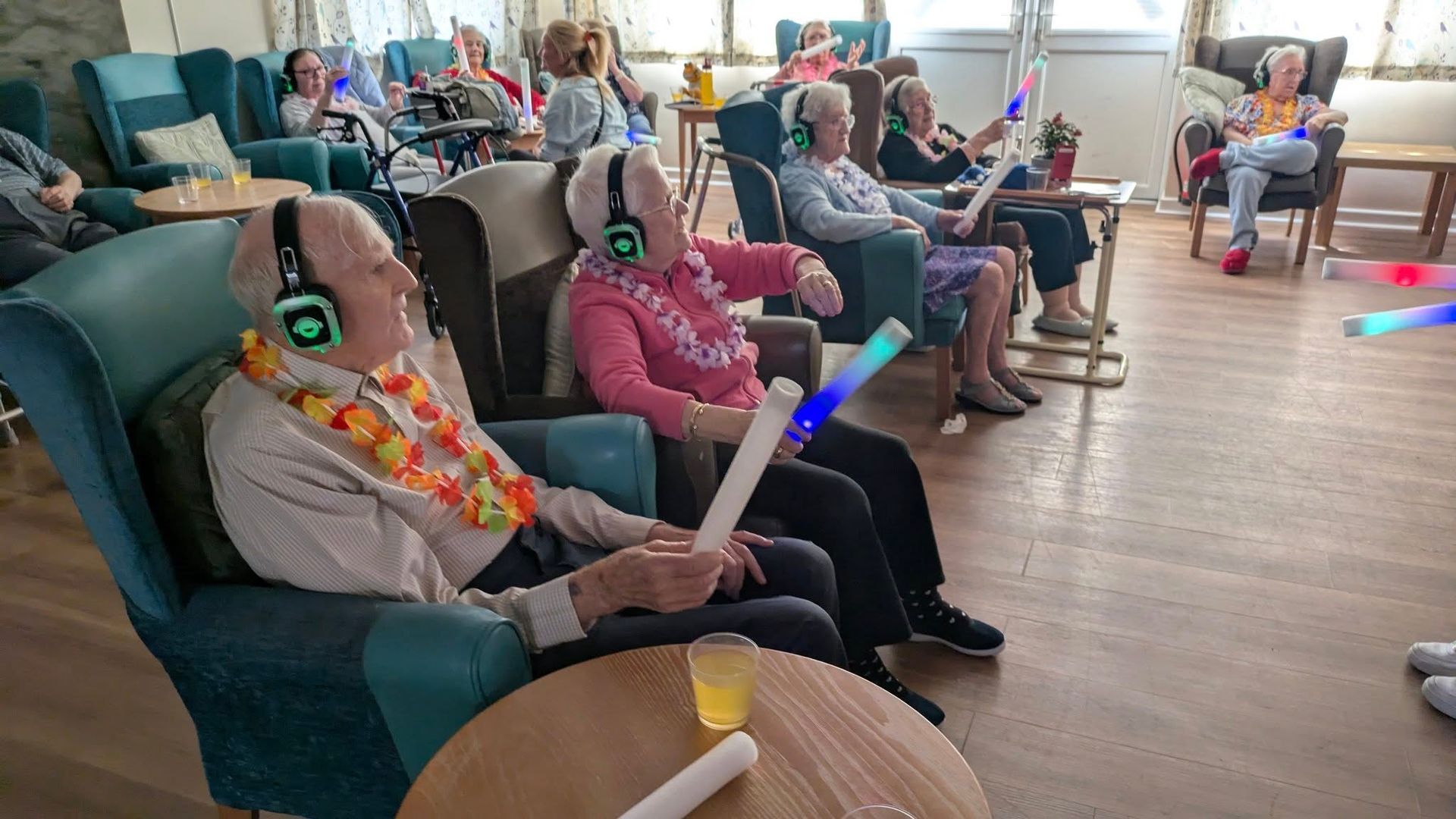 A group seated in a room, wearing headsets and holding glow sticks during a social activity.
