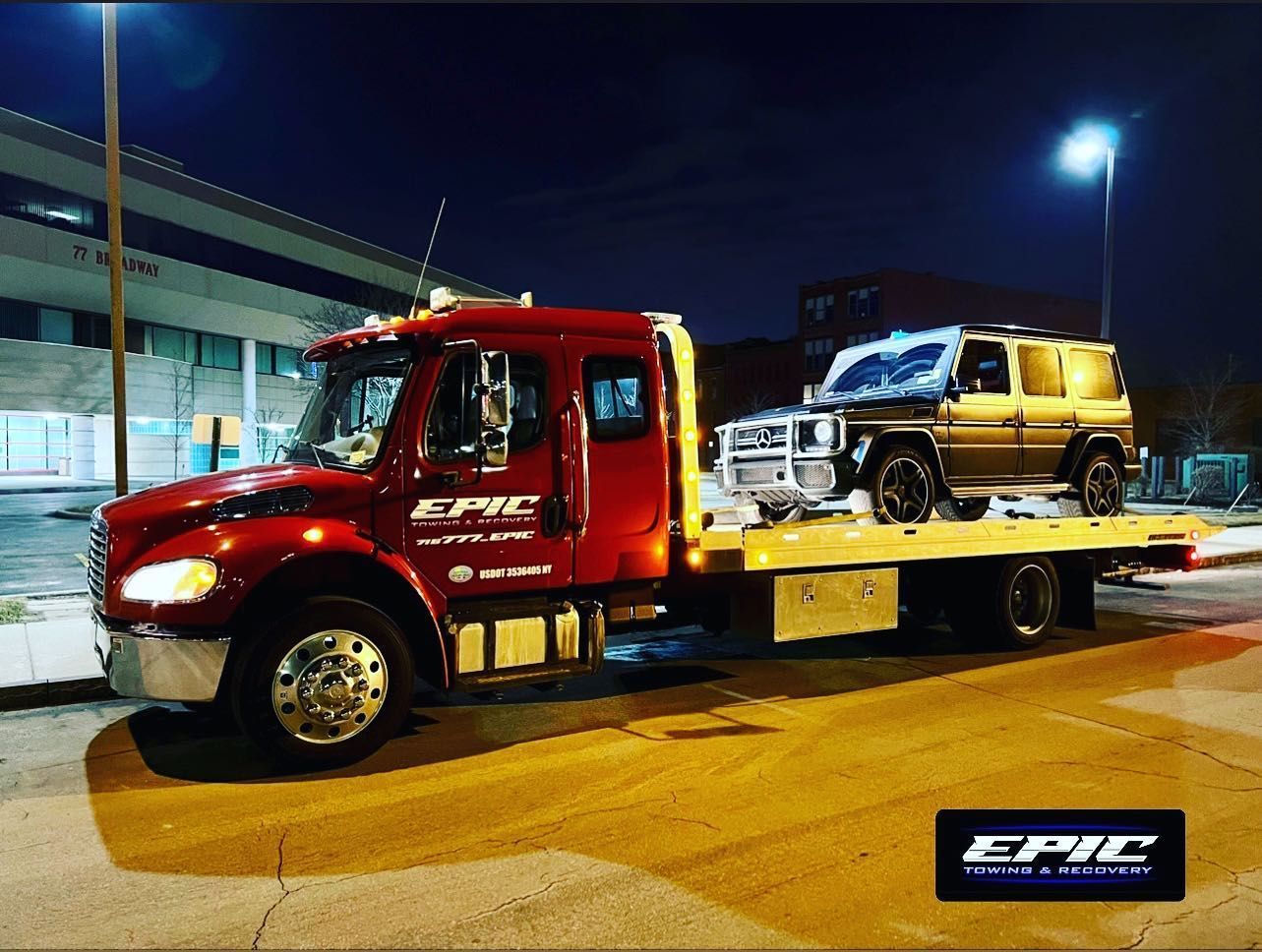 Red flatbed tow truck carrying a gold SUV at night outside a building