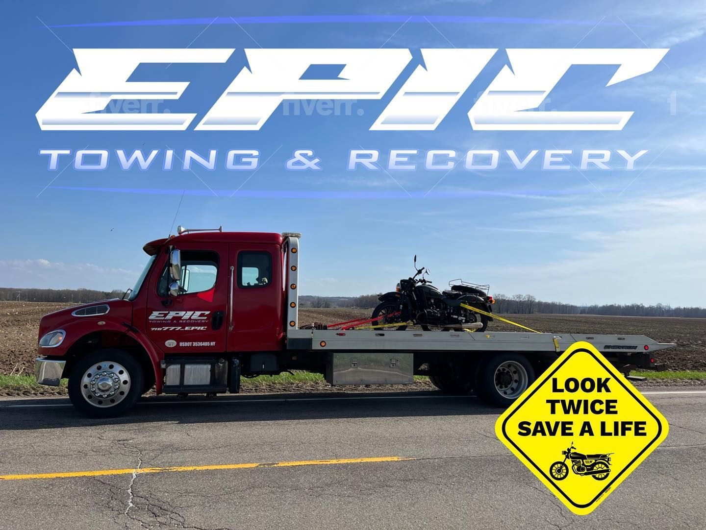 Red tow truck with motorcycle on flatbed and “Look Twice Save a Life” sign on highway