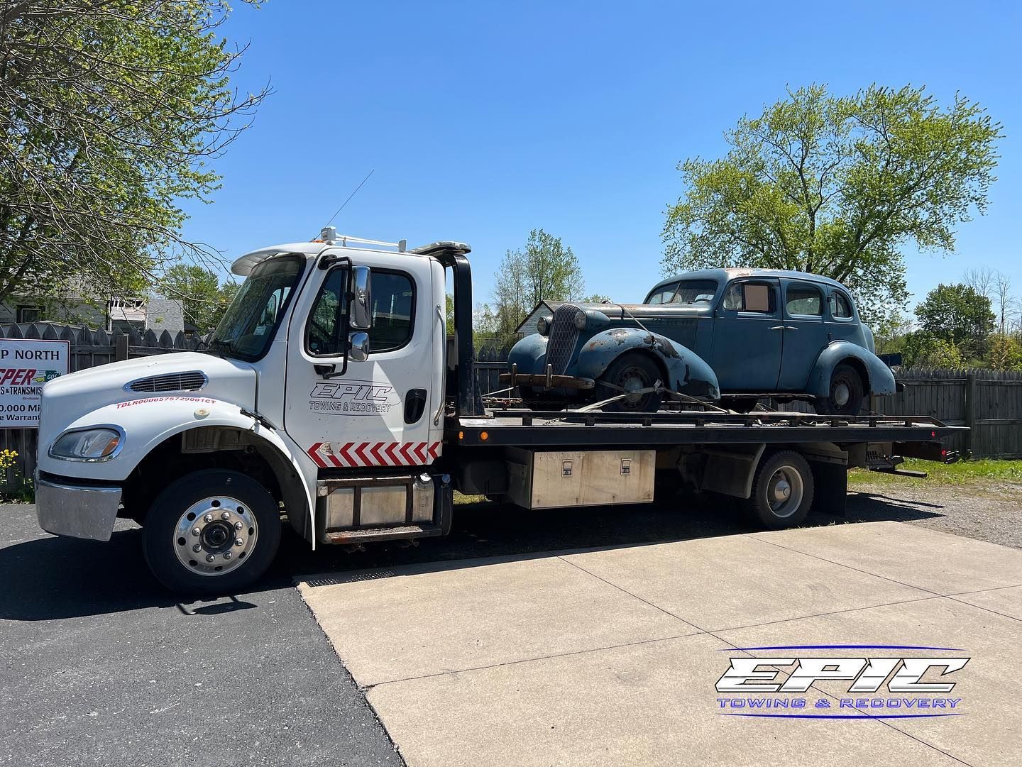 Tow truck carrying a dark blue Volkswagen Beetle on a flatbed in a sunny lot