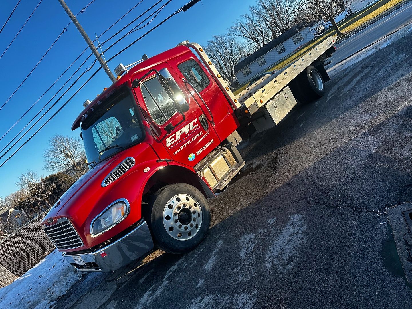 Red flatbed tow truck parked on a snowy roadside under a clear blue sky