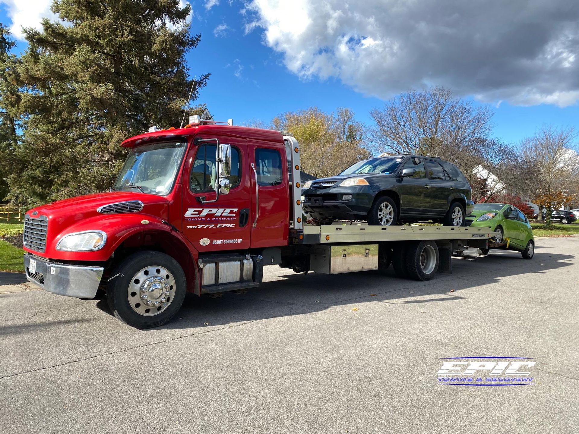 Red tow truck carrying a black car on a flatbed, parked outdoors under a blue sky.