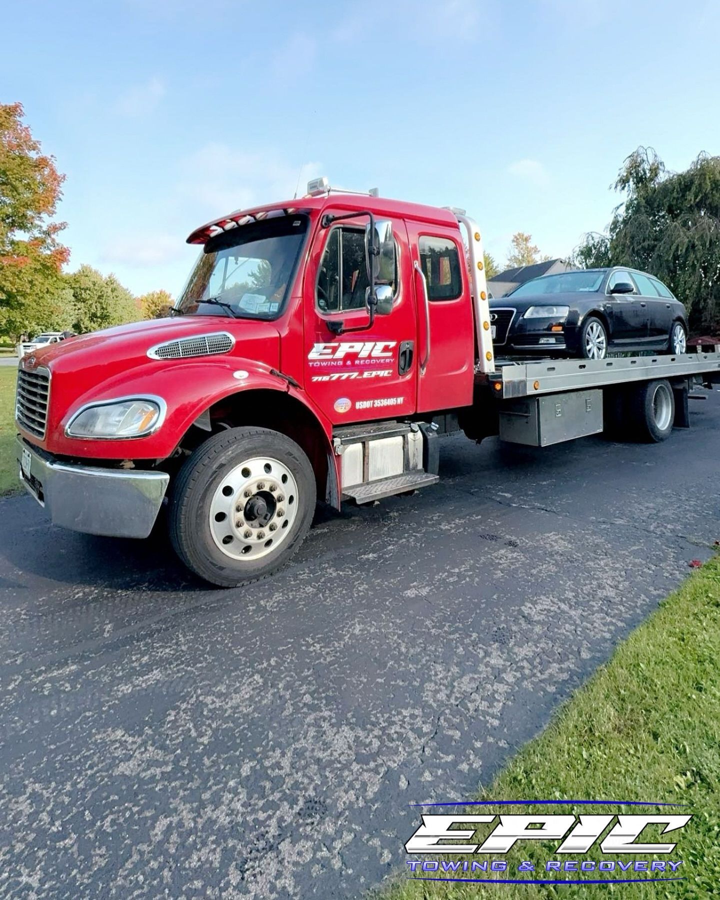 Red tow truck hauling a black sedan on a roadside under a clear sky