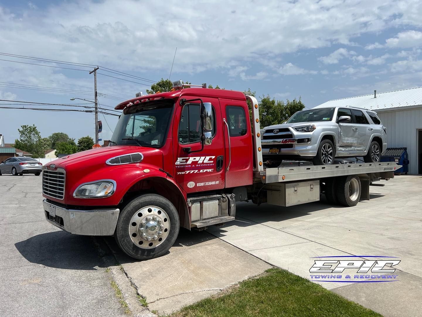 Red tow truck carrying a silver SUV on a sunny roadside.
