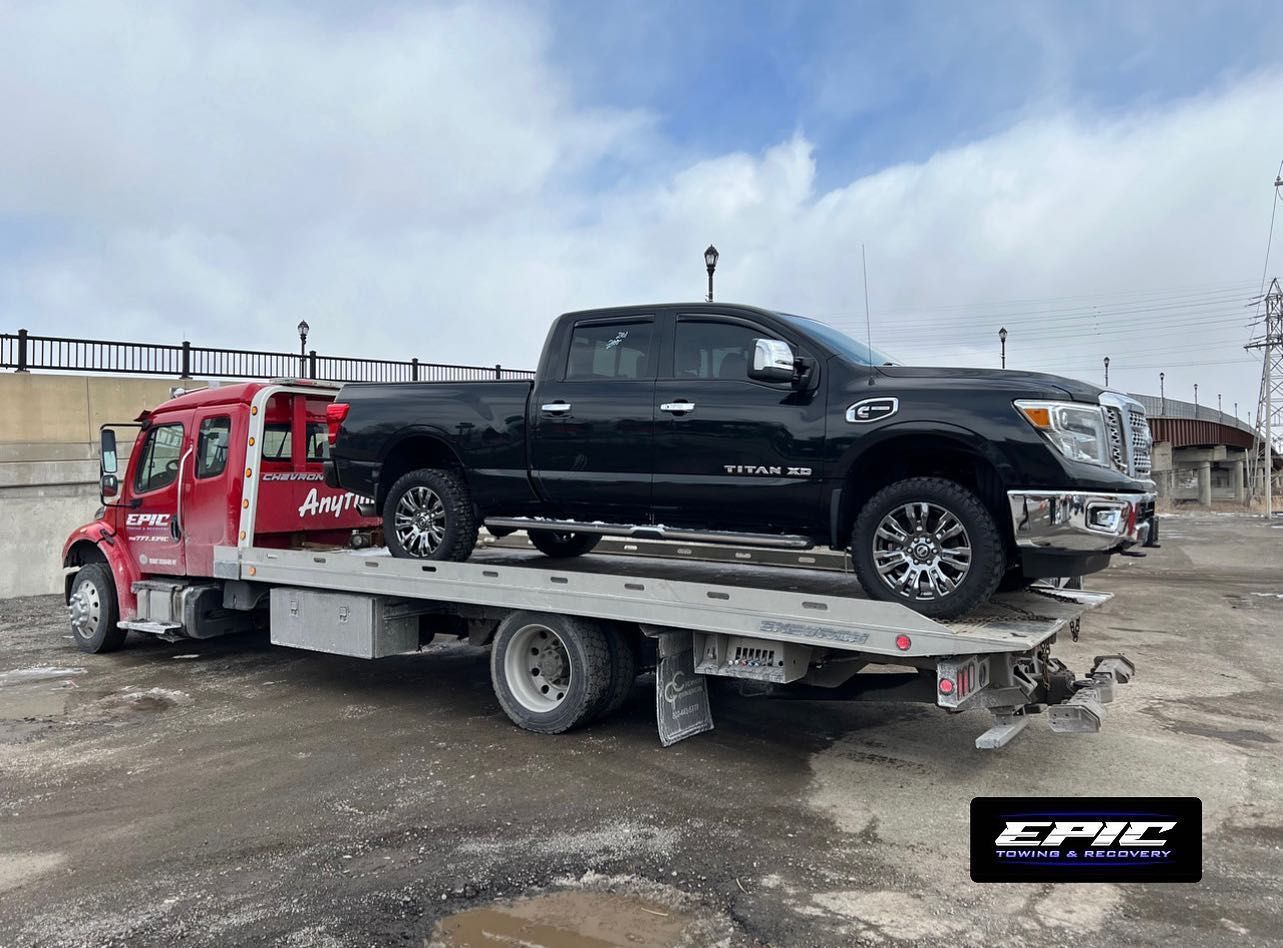 Red tow truck hauling a black pickup on a flatbed in a snowy lot