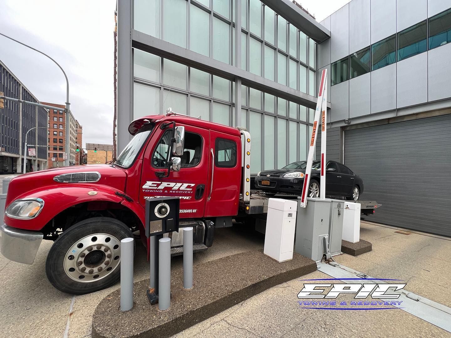 Red tow truck beside a modern building, parked at a charging station.