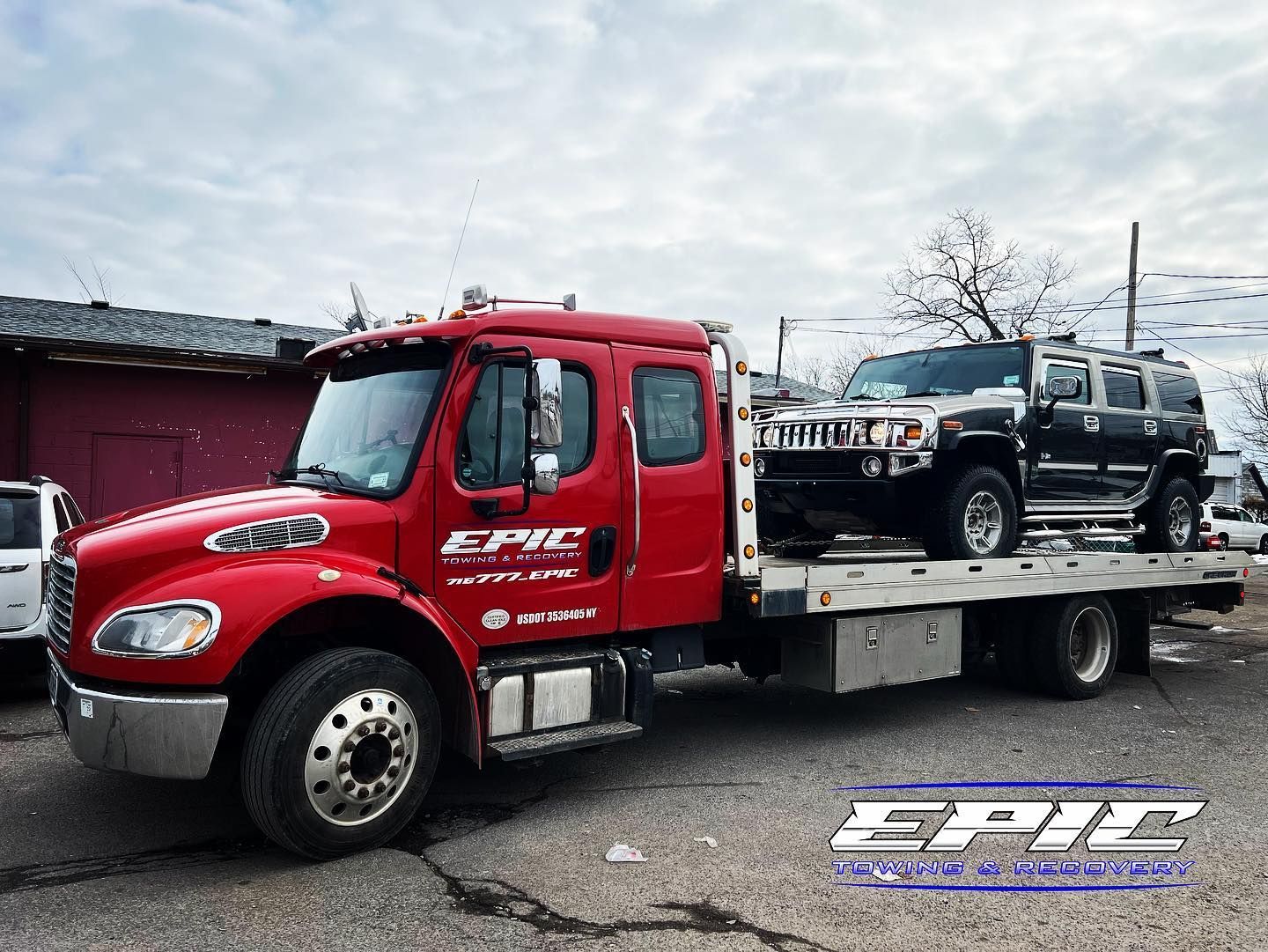 Red tow truck carrying two black SUVs on a flatbed in a lot