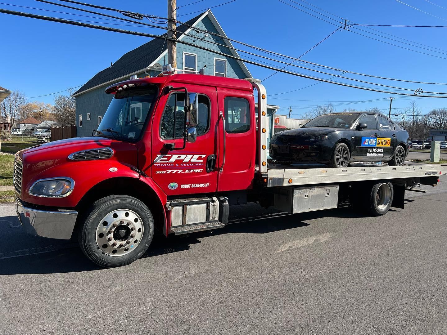 Red flatbed tow truck parked on a street under a blue sky.