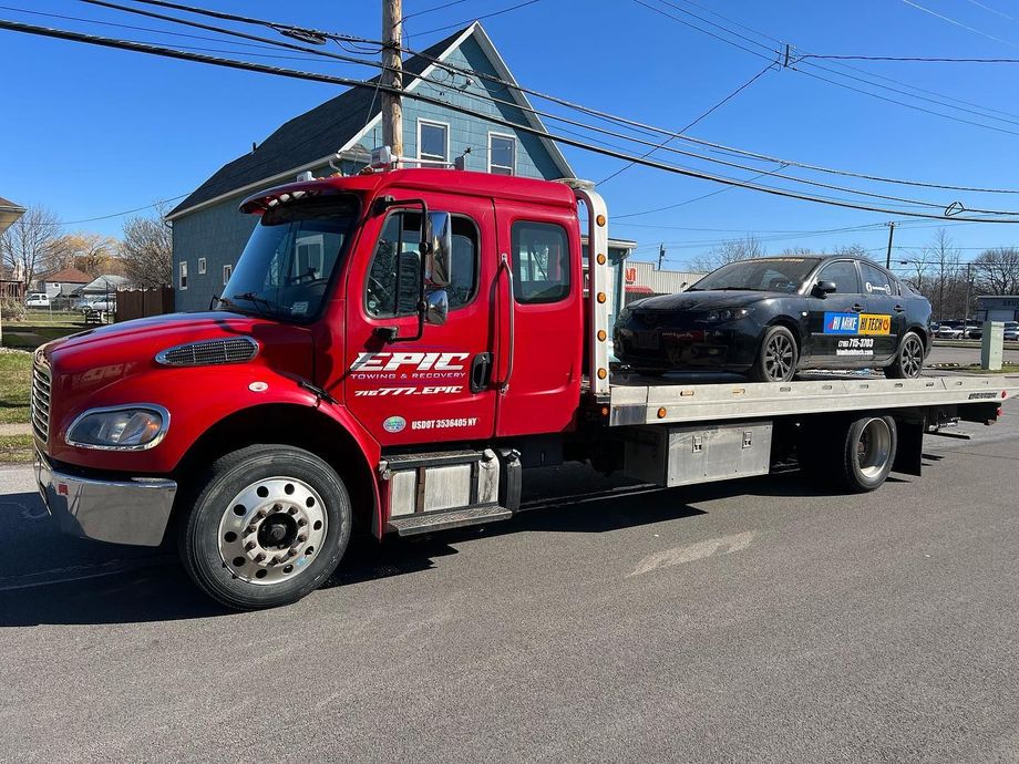 Red flatbed tow truck parked on a street under a blue sky.