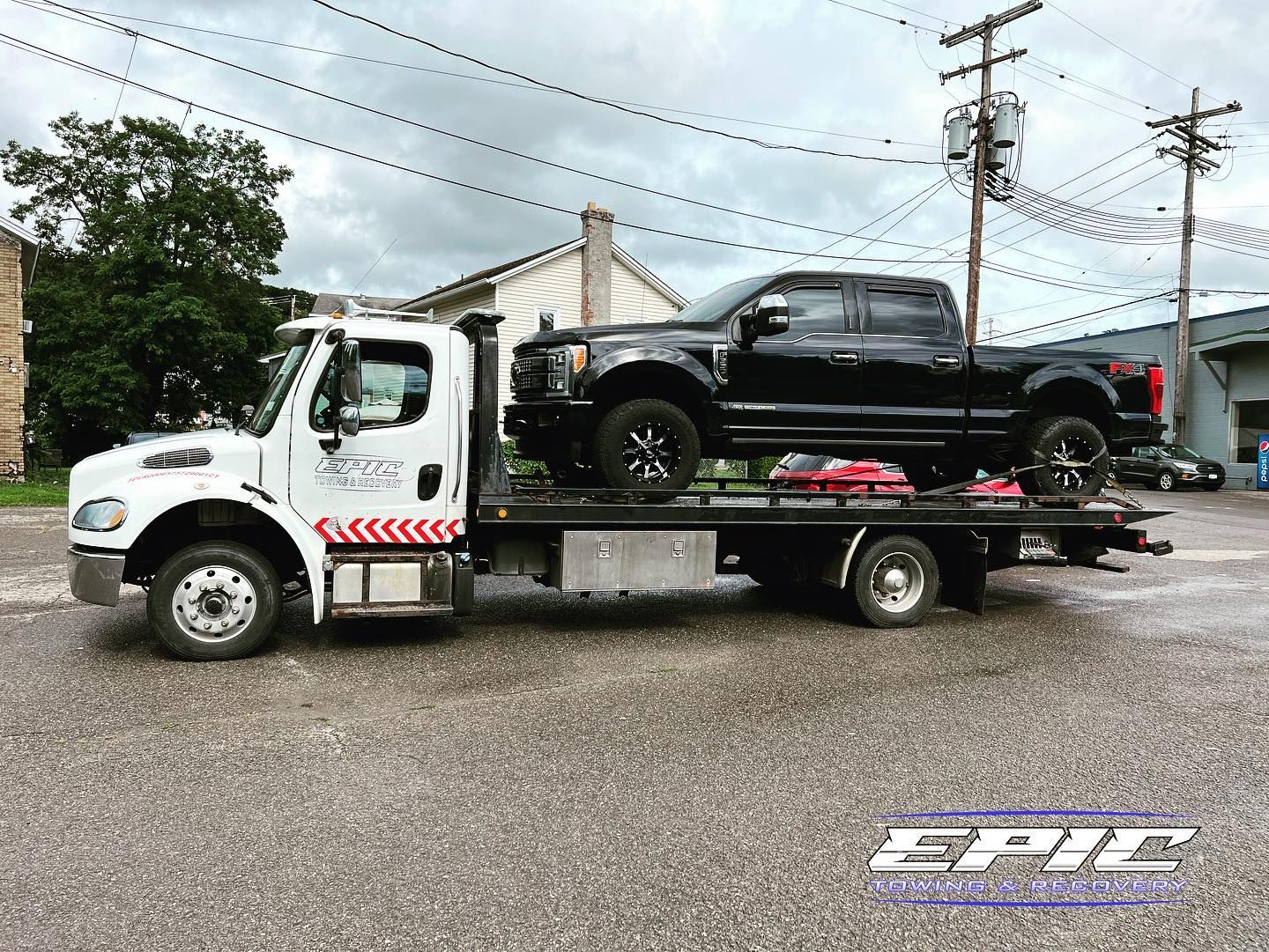 Tow truck hauling a black pickup truck on a flatbed in a gravel lot