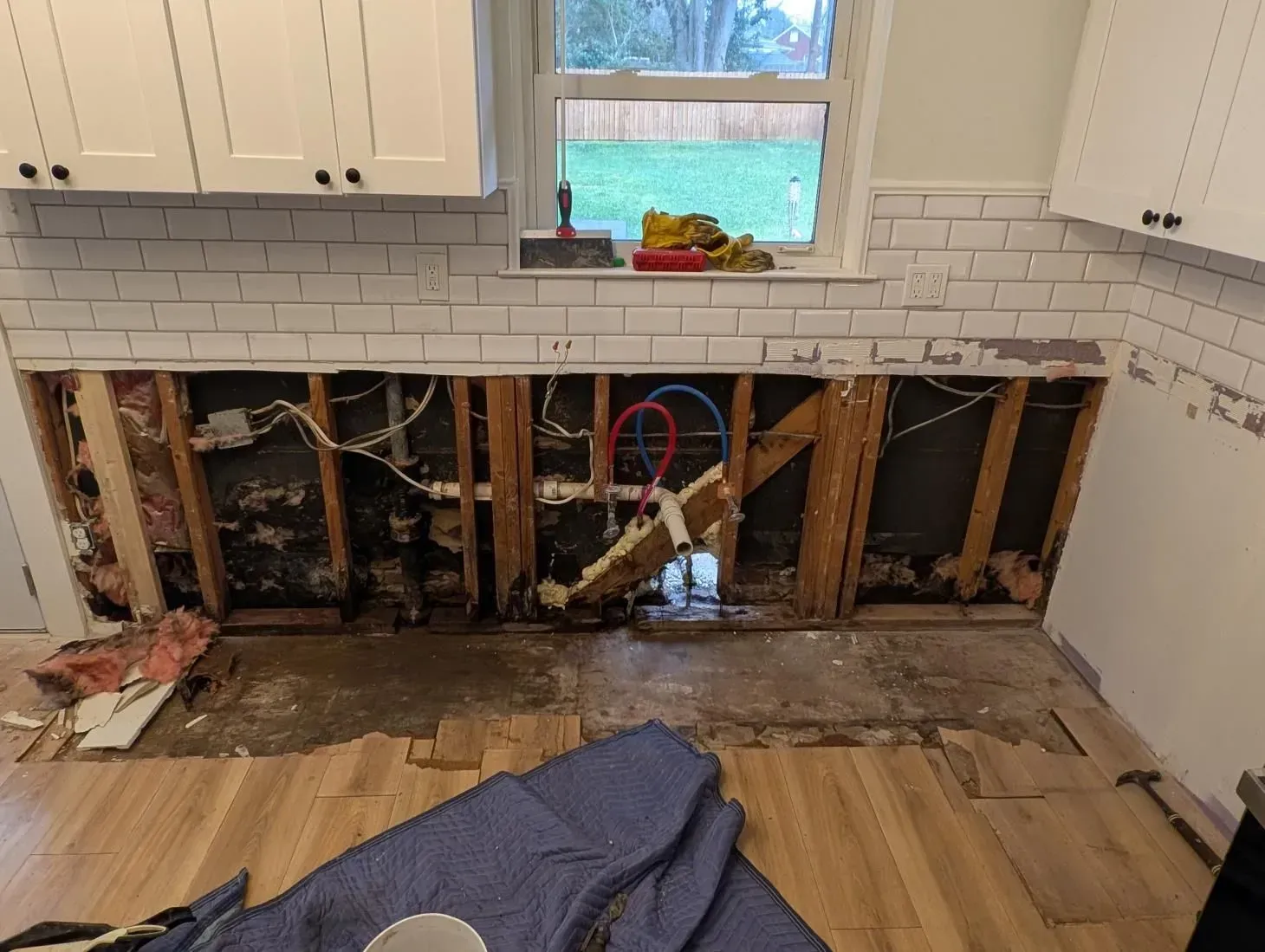 A kitchen with a hole in the wall and a blue blanket on the floor.