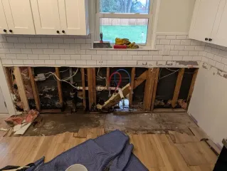 A kitchen with a hole in the wall and a blue blanket on the floor.