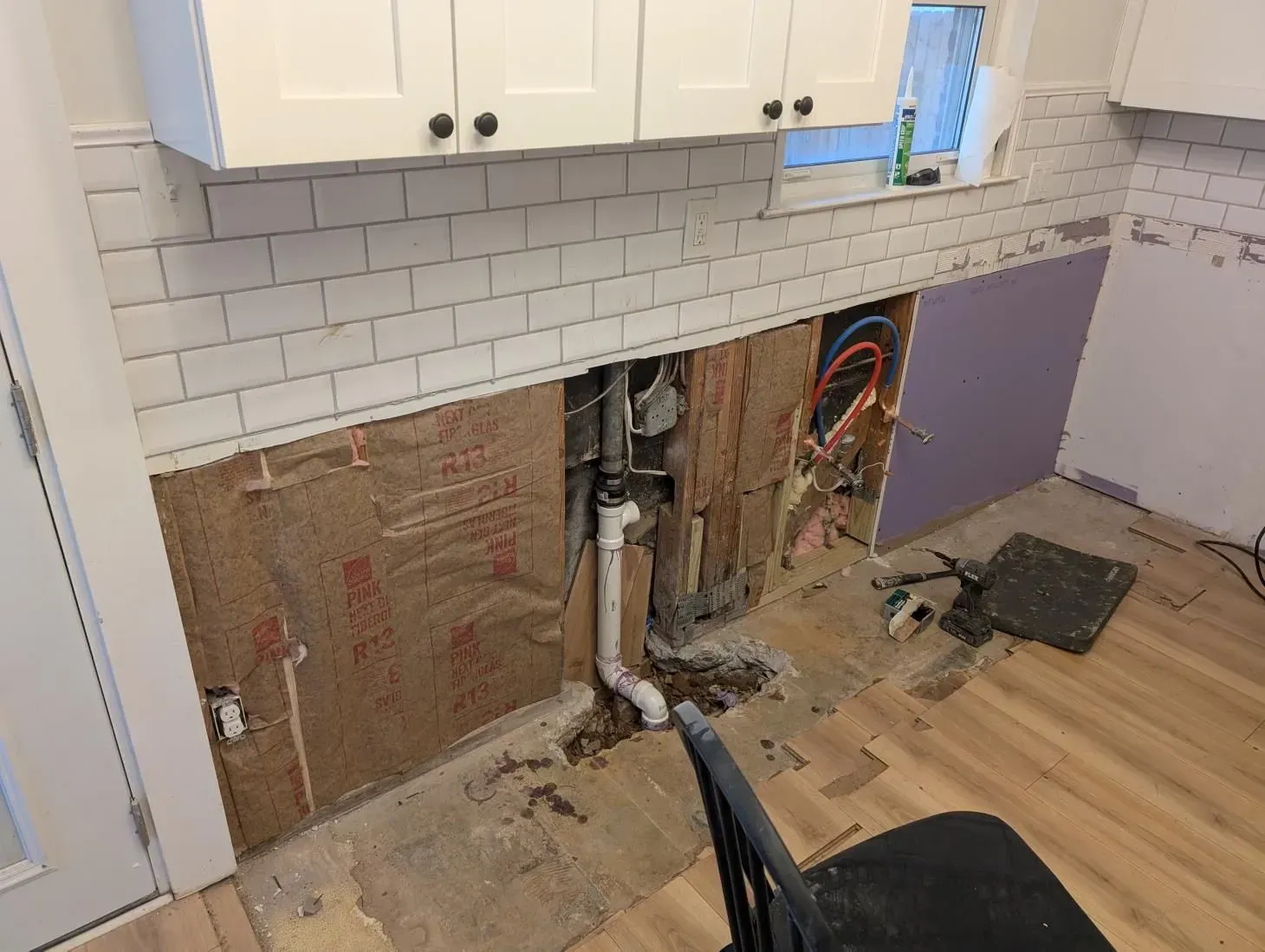 A kitchen with a hole in the wall and a chair.