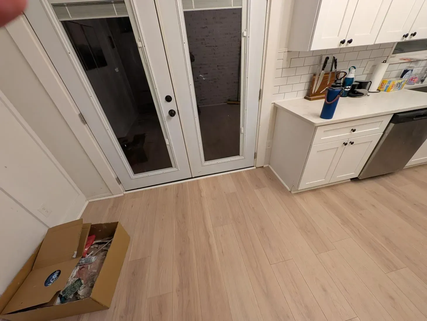 A kitchen with white cabinets and stainless steel appliances and a cardboard box on the floor.