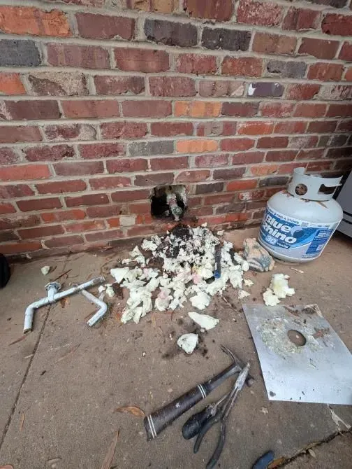 A propane tank is sitting on the ground next to a brick wall.