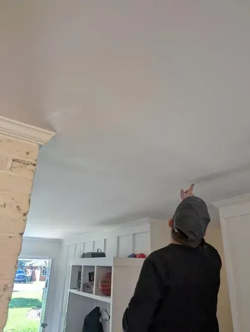A man is standing in a living room looking up at the ceiling.