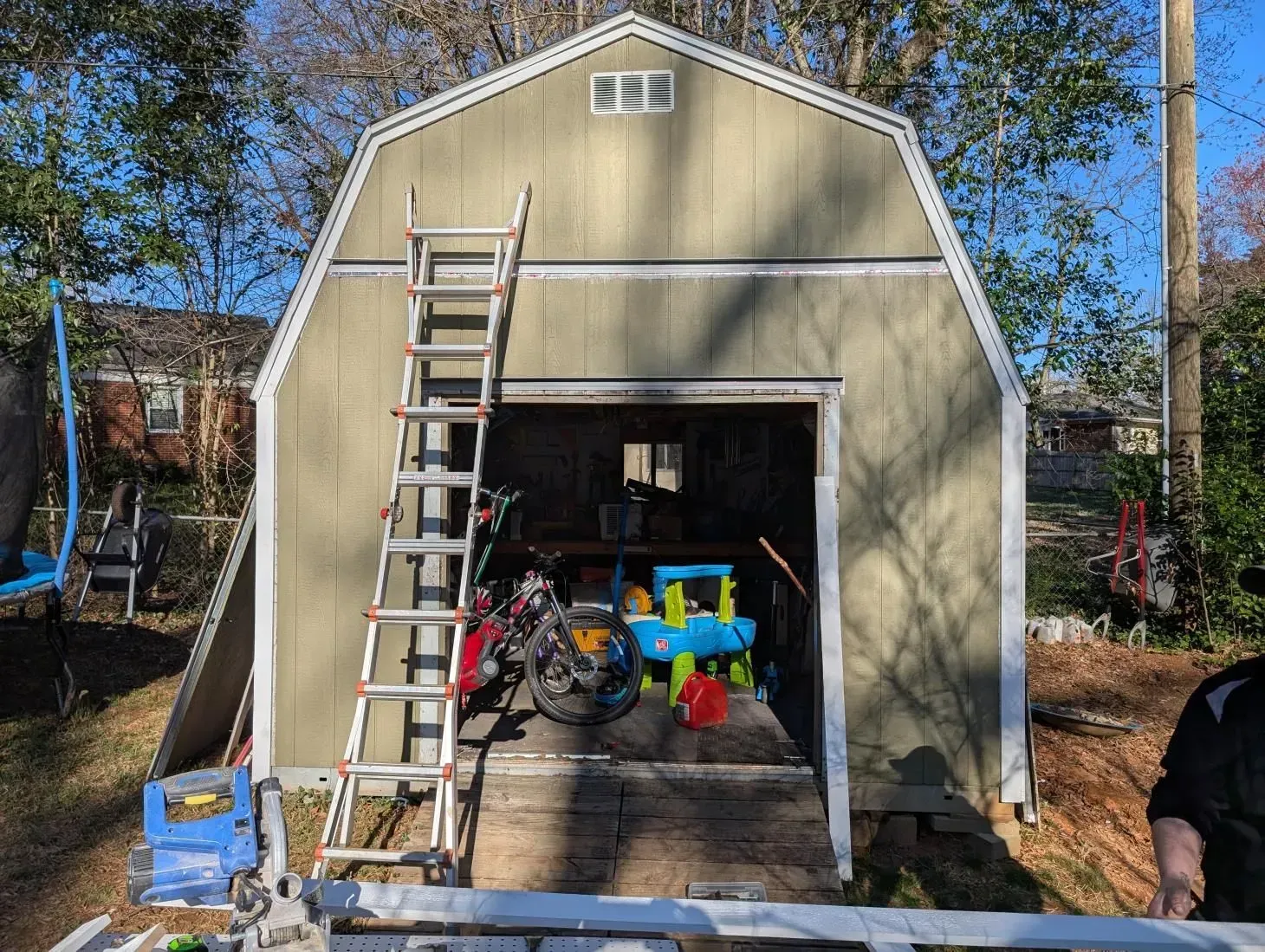 A man is standing in front of a garage with a ladder in it.