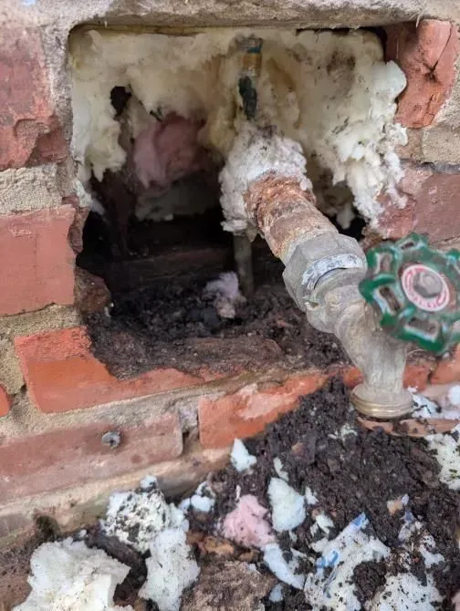 A water pipe is coming out of a hole in a brick wall.