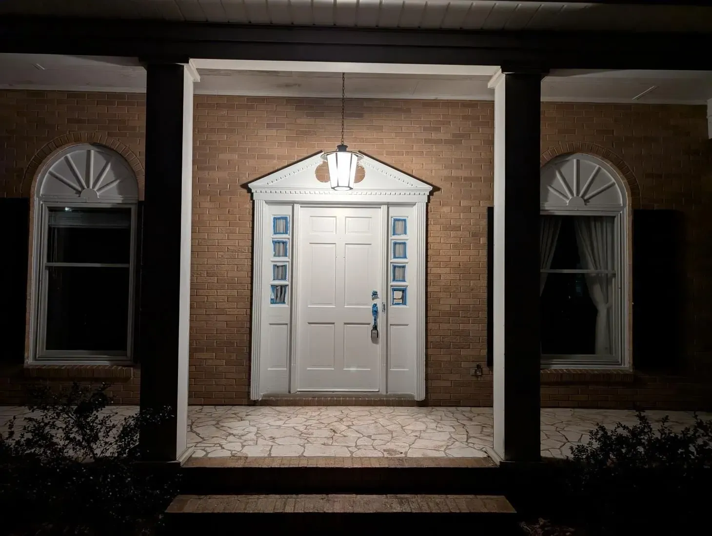 The front door of a brick house is lit up at night.
