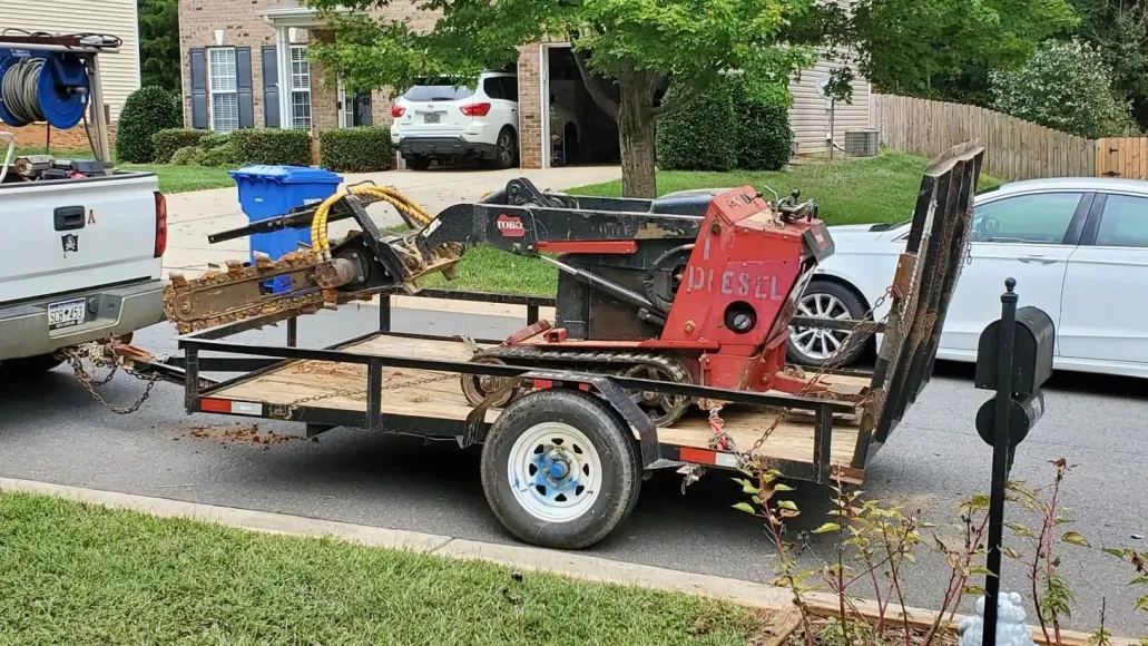 A trailer with a machine on it is parked in front of a house.