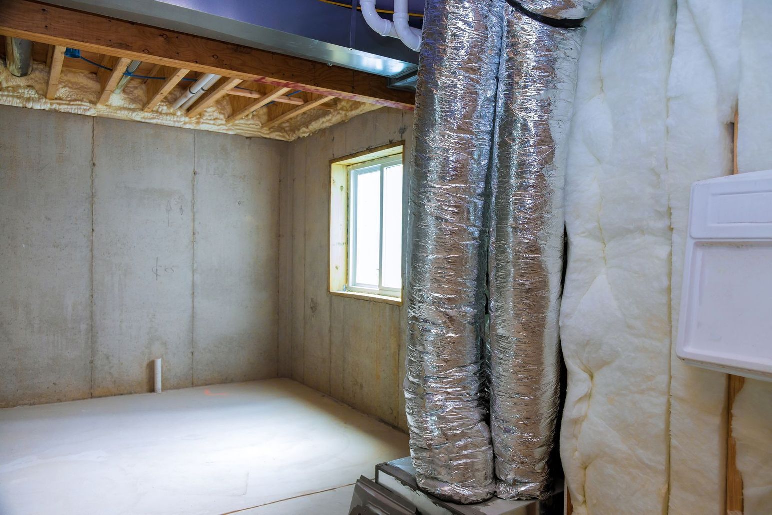 An empty basement with a window and air ducts.