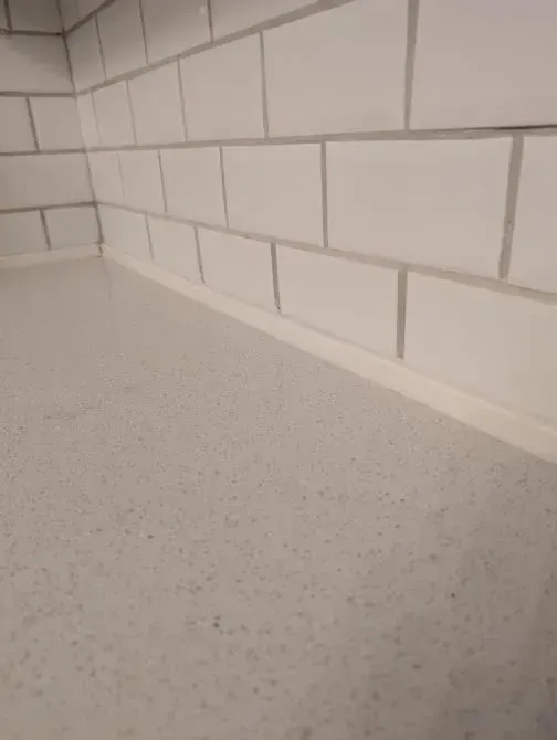 A white tile wall with a white counter top in a kitchen.