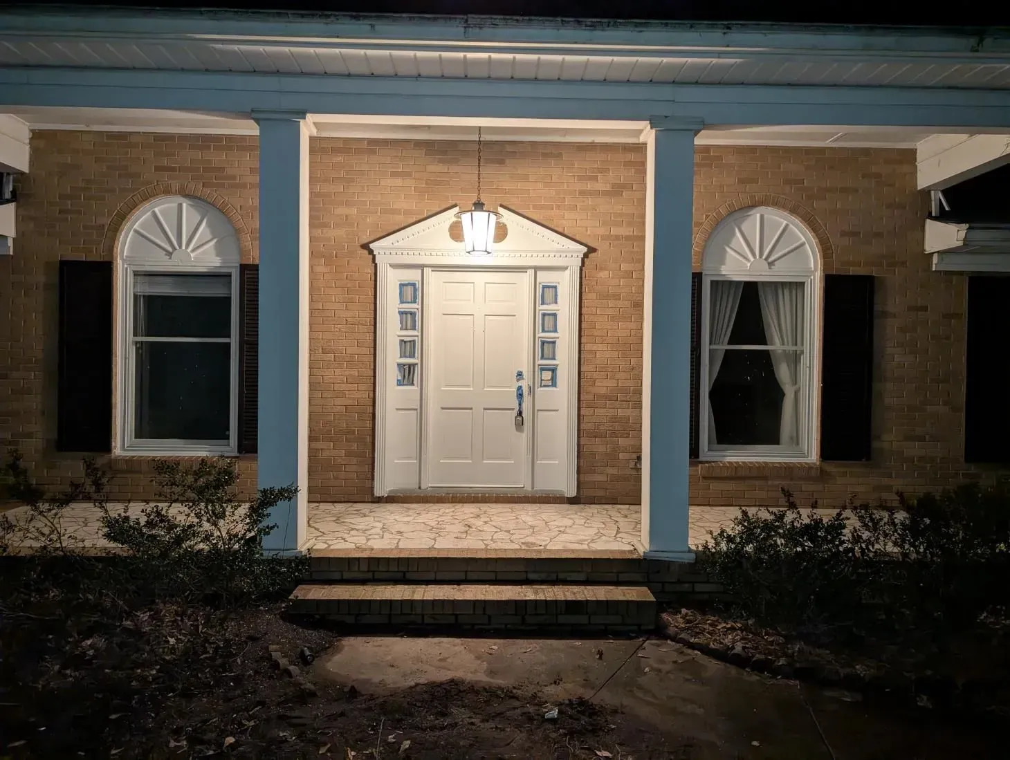 A brick house with a white door and a blue porch at night.