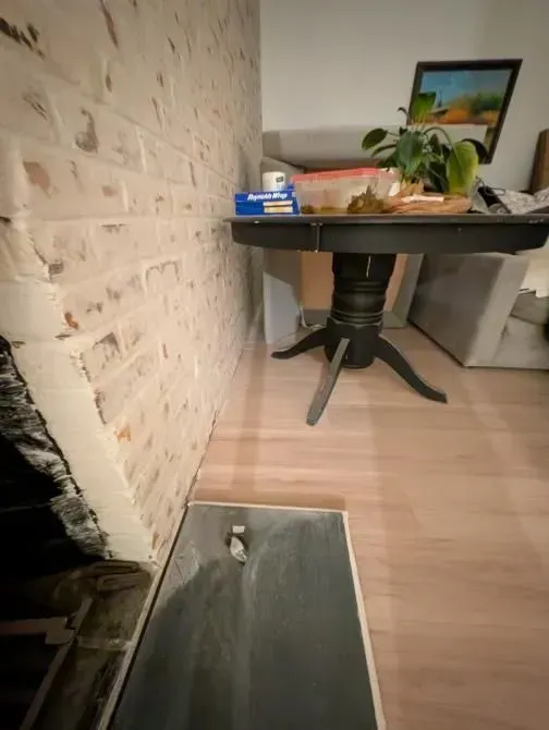 A table with a plant on it is in a living room next to a brick wall.