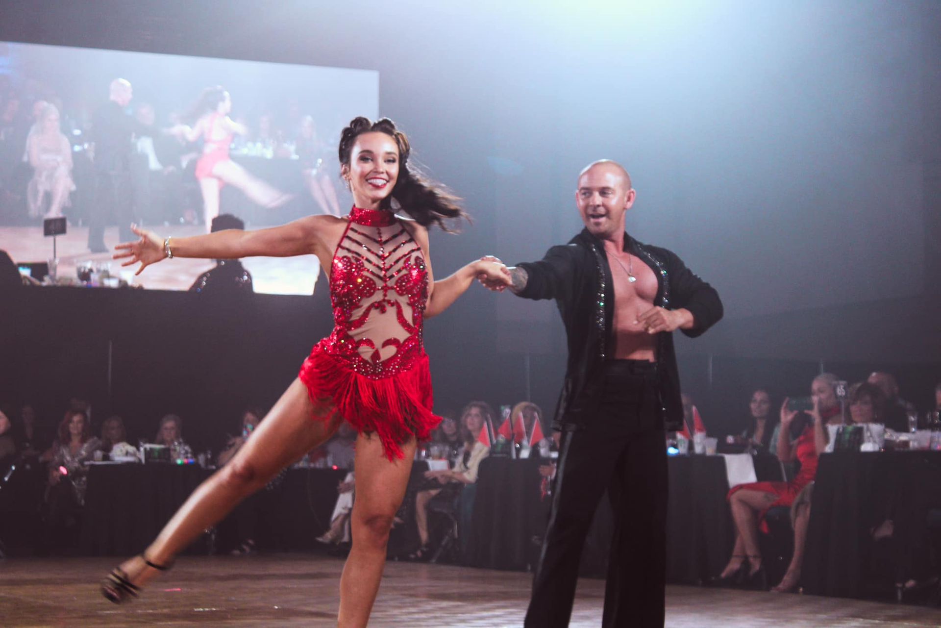 Two ballroom dancers performing a lively routine in a spotlighted competition hall