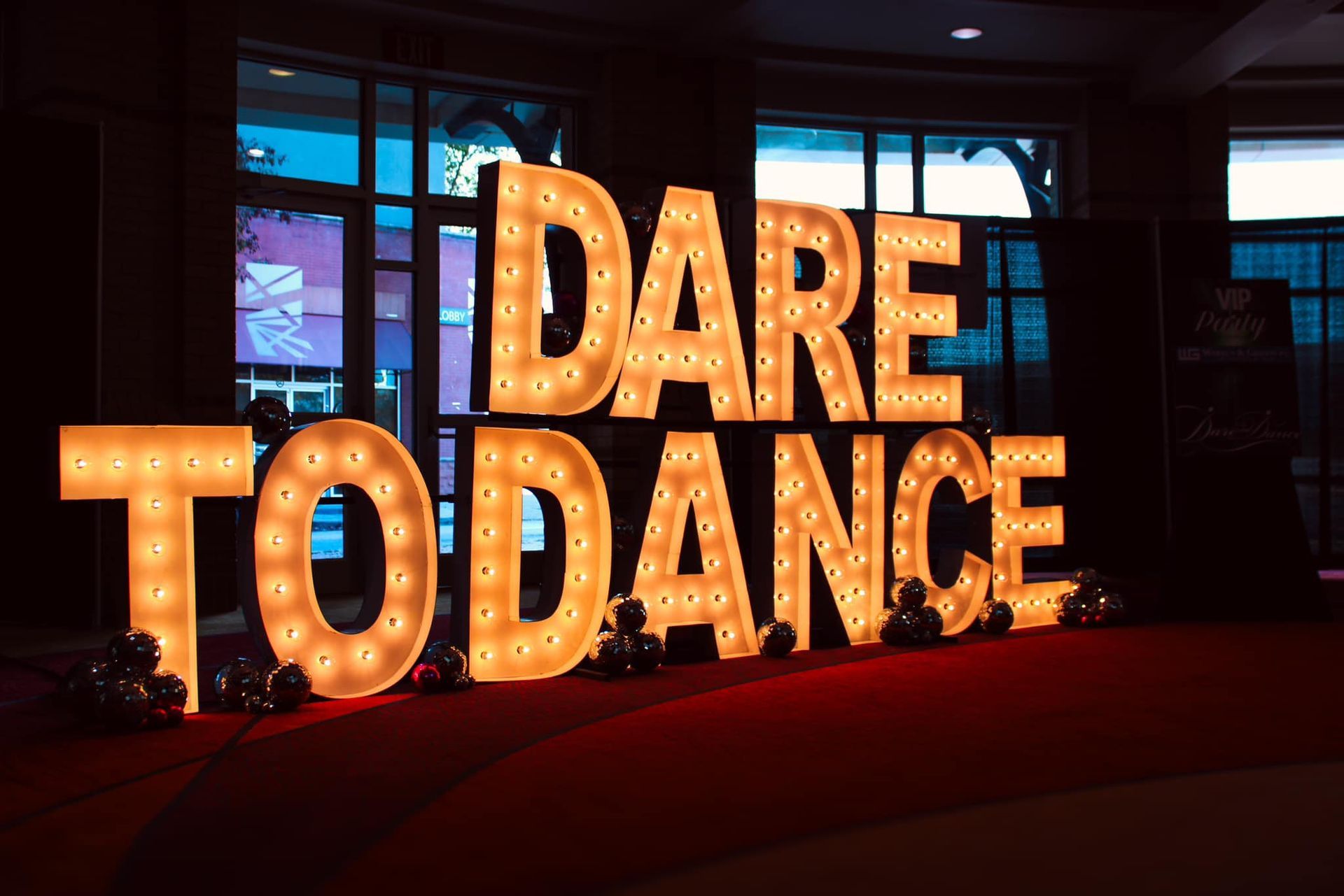 Large lit marquee letters reading “DARE TO DANCE” in a dim indoor venue