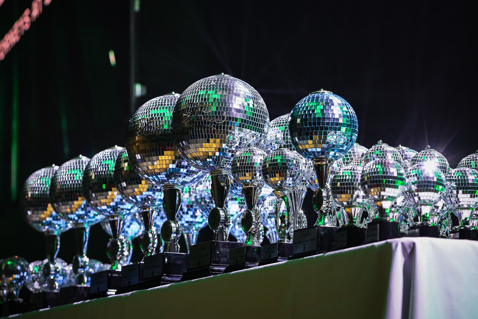 Row of mirrored trophy-like spheres on a table, reflecting colorful lights in a dark setting