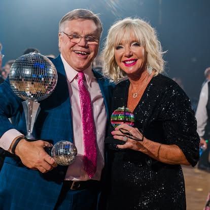 Two smiling people in glittery outfits holding disco balls at a party.