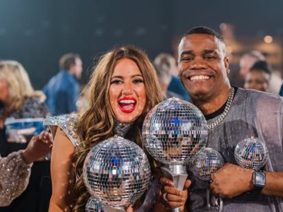 Two people smiling and holding silver disco-ball trophies at an awards event