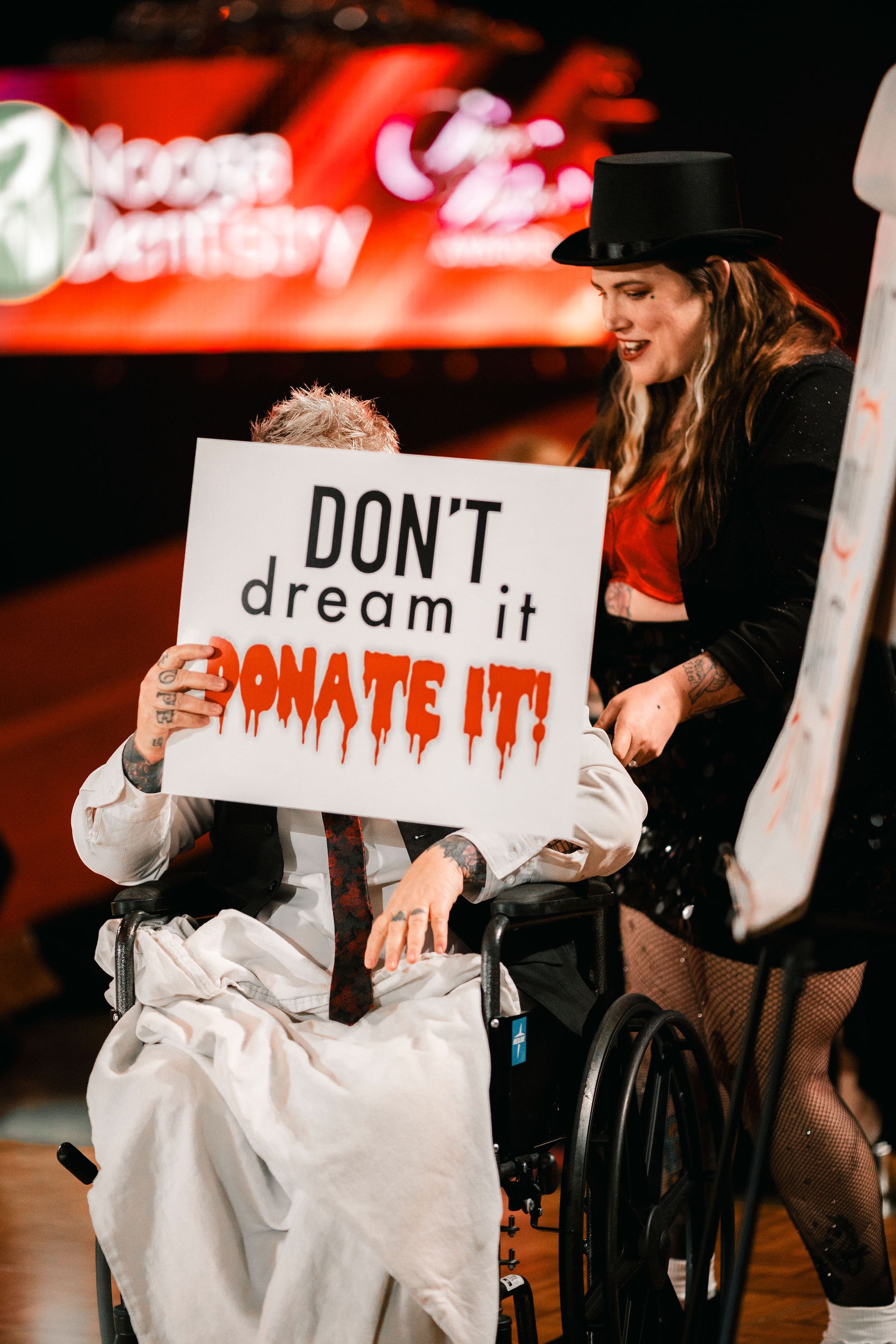 Protester holding a sign reading “DON’T dream it, DO IT!” while another stands nearby in a top hat.