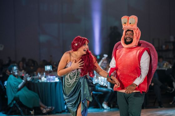 Two performers in colorful costumes dancing on a stage at a lively event