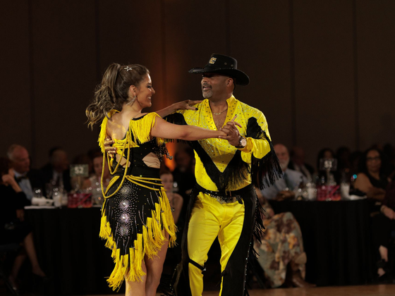 Two ballroom dancers in yellow and black costumes performing on a dance floor