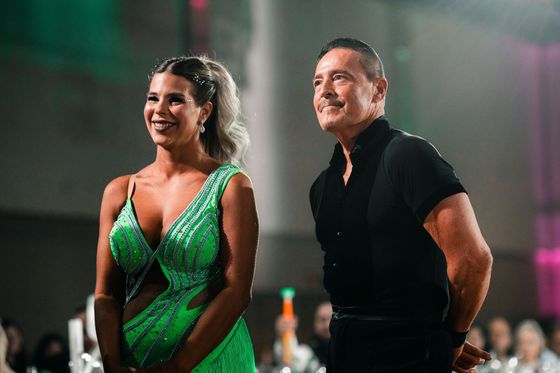 Two smiling people standing in a ballroom, one in a green dress and one in a black shirt