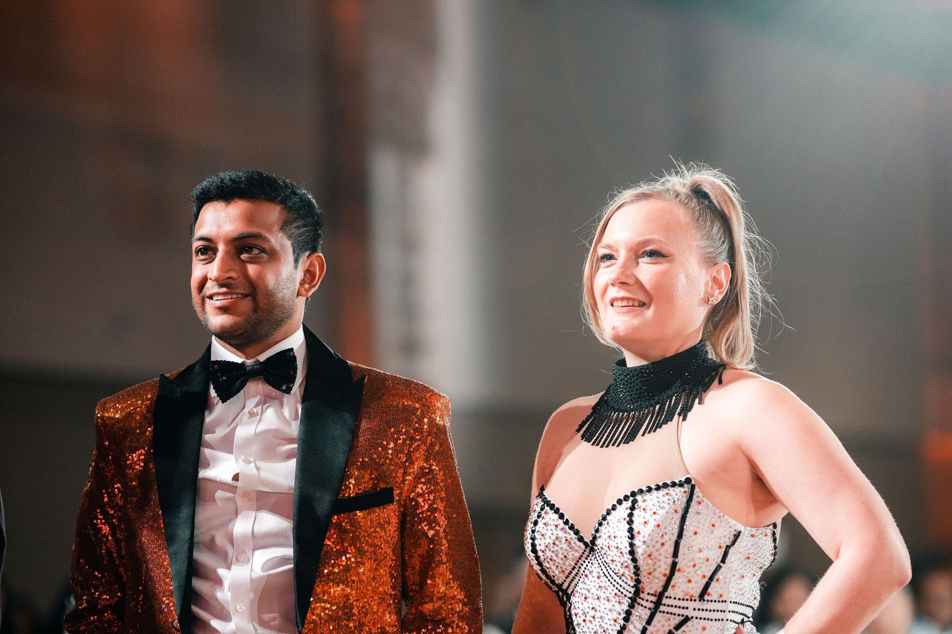Two performers in sparkly stage costumes smiling under warm lights