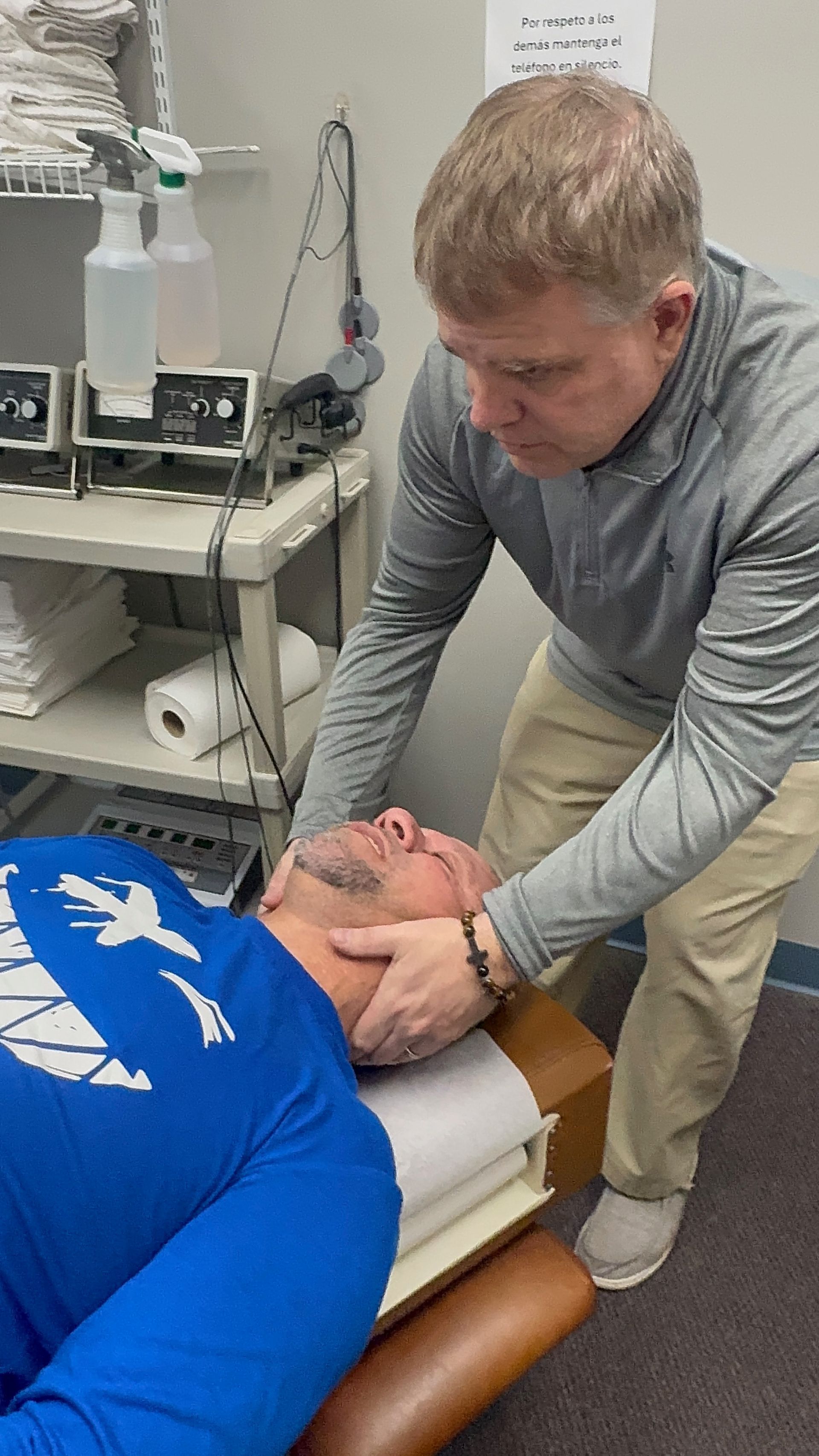 Chiropractor adjusting a patient's neck. Patient lies on a table, doctor has hands on head. Clinic setting.